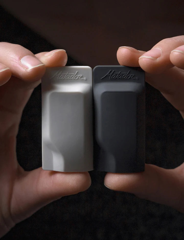 Two small rectangular devices, one gray and one black, held between fingers against a dark background.