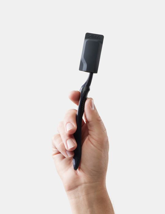 Hand holding a black toothbrush with caps against a light gray background