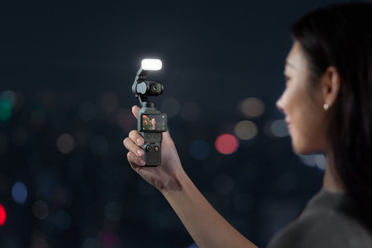 Person holding a dji osmo pocket 4 with a fill light on a dark background