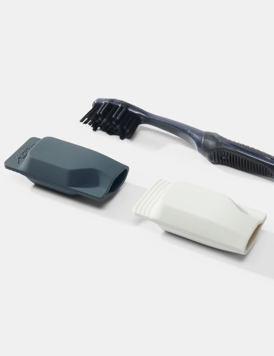 A dark gray toothbrush with black bristles, shown with two interchangeable silicone heads in dark gray and white on a light gray background.
