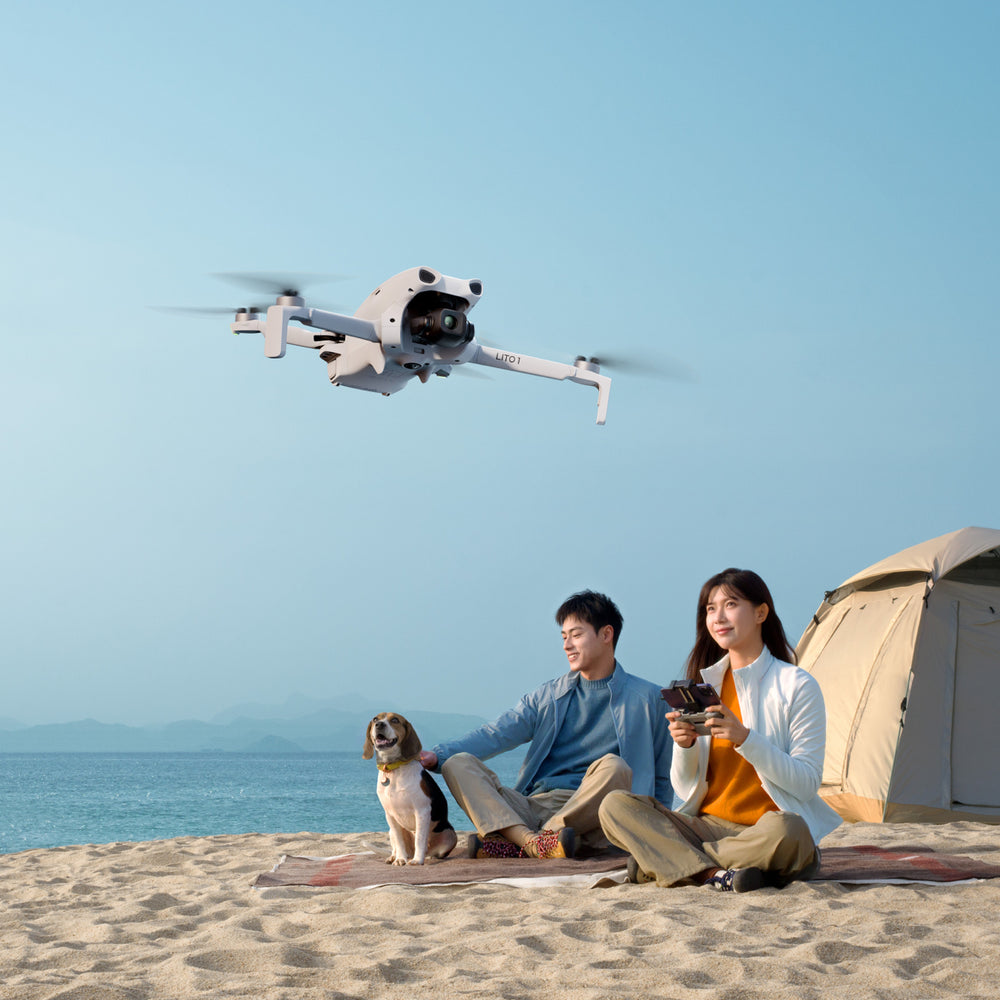Two people sitting on a beach with a drone and a tent in the background