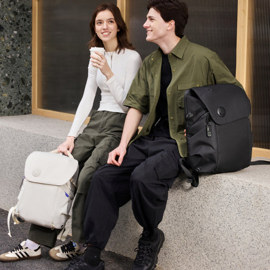 Two people sitting on a ledge with backpacks, one holding a coffee cup.