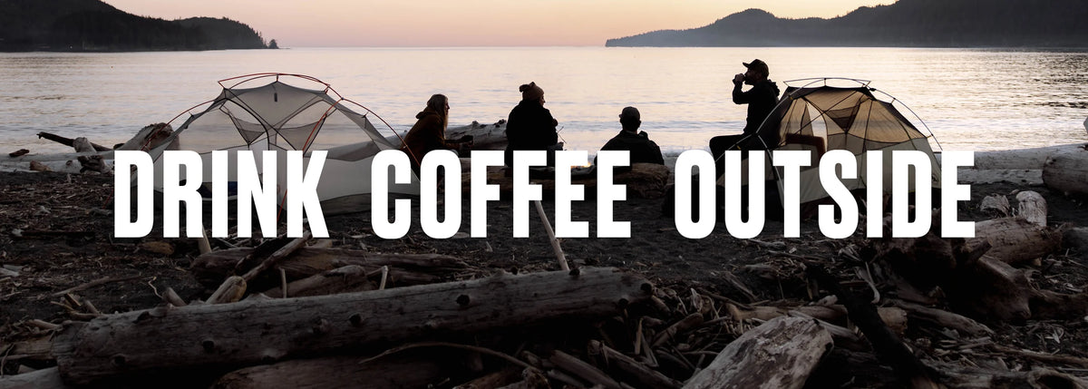 A scenic outdoor coffee break at dusk on a rocky shoreline, with silhouetted people sitting between two dome tents. Large white text across the center reads “DRINK COFFEE OUTSIDE.