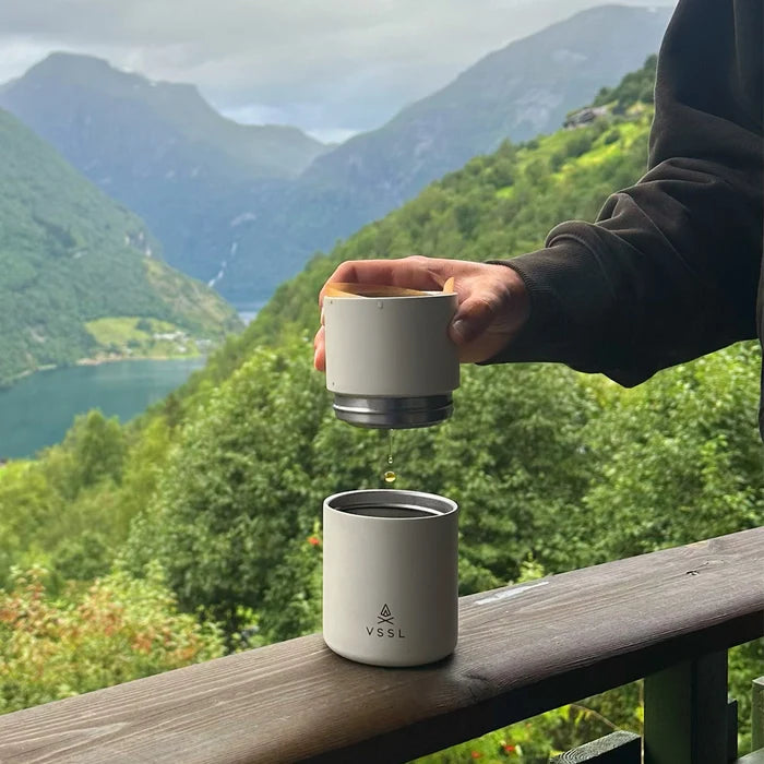 Person holding a VSSL travel mug with a scenic mountain view in the background