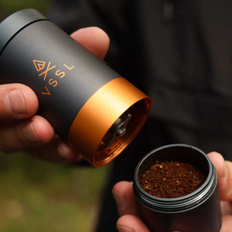 Person holding a portable coffee grinder with ground coffee visible