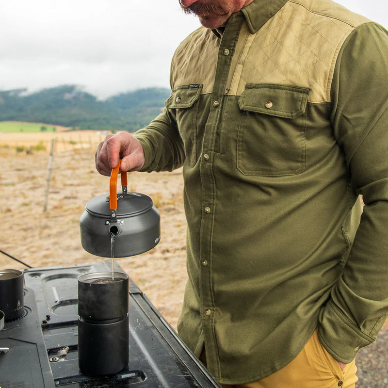 Man in green shirt pouring from a black kettle outdoors