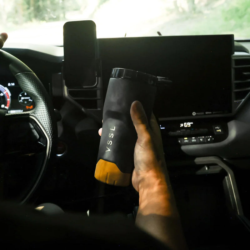 Hand holding a black insulated mug with 'TSSA' branding inside a car.