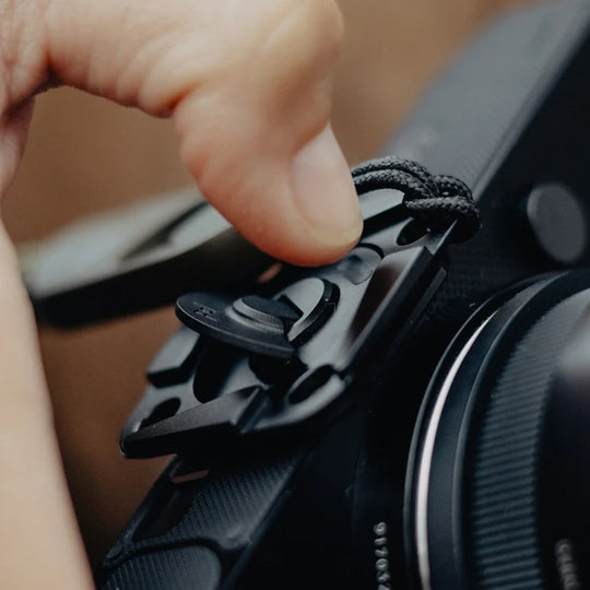 Person adjusting a strap on a camera with a blurred background