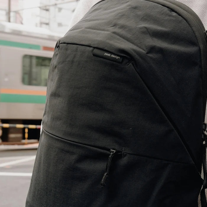 A close-up of a black backpack with a zippered pocket and a small &