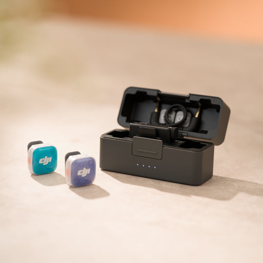 DJI Mic Mini 2S charging case sitting open next to two wireless transmitter units with colorful teal and purple magnetic front covers attached.