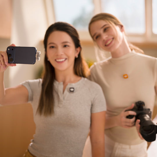 Two female content creators recording video using a smartphone equipped with a DJI Mic Mini 2S mobile receiver and clip-on wireless transmitters.