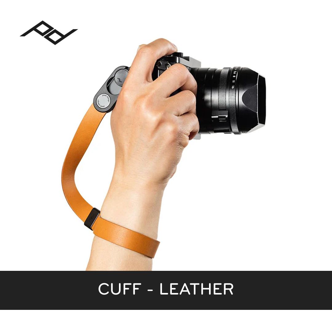 Hand holding a camera with an orange leather cuff on a white background