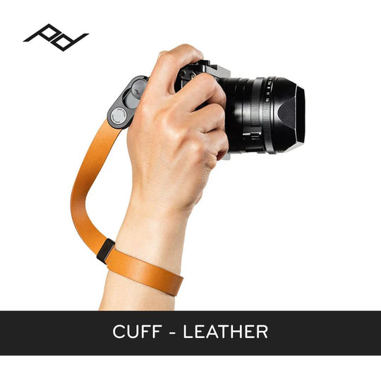 Hand holding a camera with an orange leather cuff on a white background
