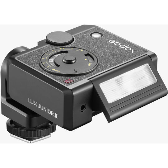 Three-quarter angle view of the Godox Lux Junior II Retro Camera Flash with its flash head tilted upward, showing the top exposure control dial, textured leatherette finish, and sync port.