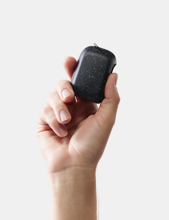 Hand holding a small black device with a textured surface against a light background