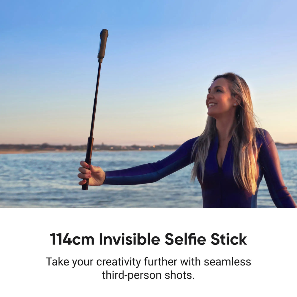 Woman holding the extended Insta360 114cm Invisible Selfie Stick with a 360 action camera by the ocean for third-person action perspectives.