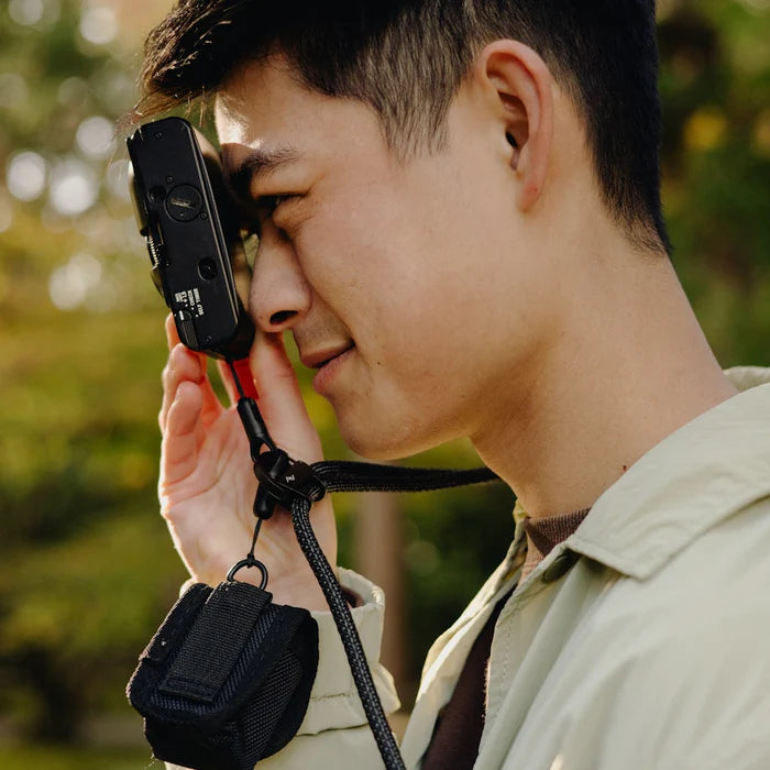 Person holding a camera with a strap over their shoulder outdoors