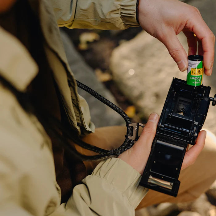 Person holding a camera with film loaded, outdoors.