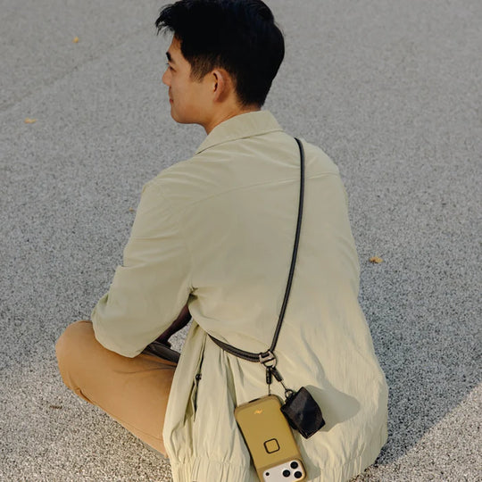 Person sitting on the ground wearing a light-colored shirt and beige pants, with a crossbody strap.