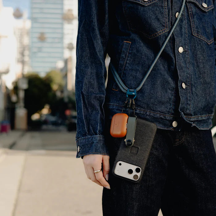 Person wearing a denim jacket with a phone case hanging from a lanyard on a city street.