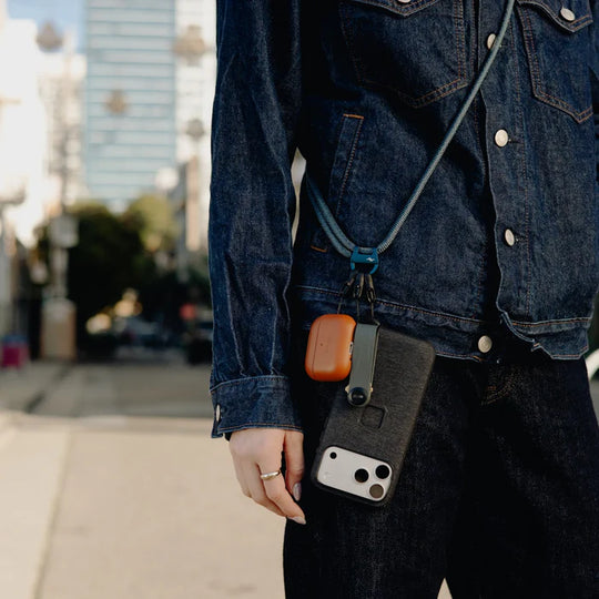 Person wearing a denim jacket with a phone case hanging from a lanyard on a city street.