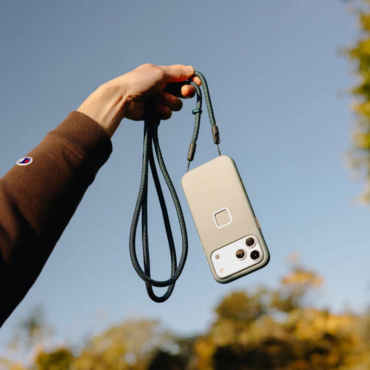 Phone case with lanyard held by a hand against a blurred natural background