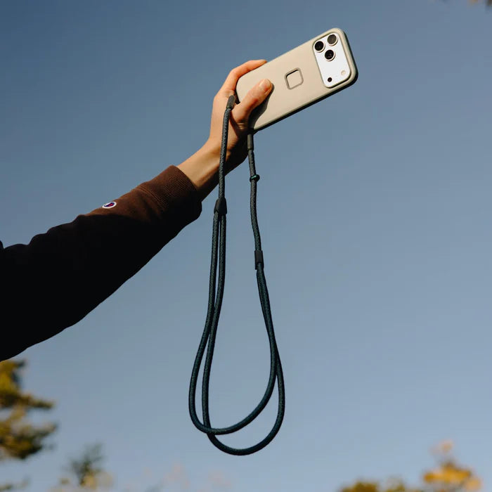 Hand holding a phone with a lanyard against a clear blue sky