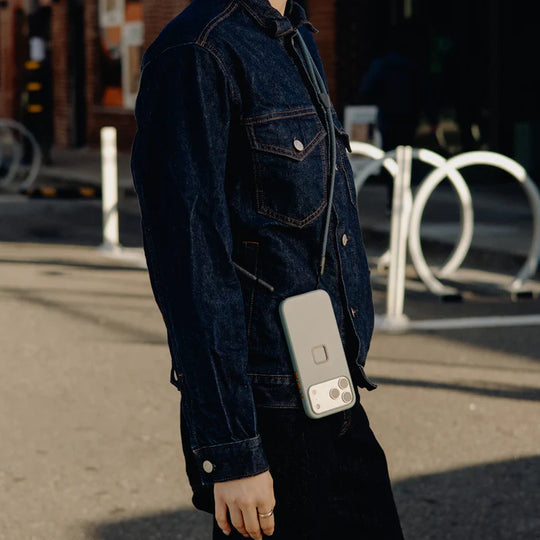 Person wearing a denim jacket holding a phone with a case outdoors.