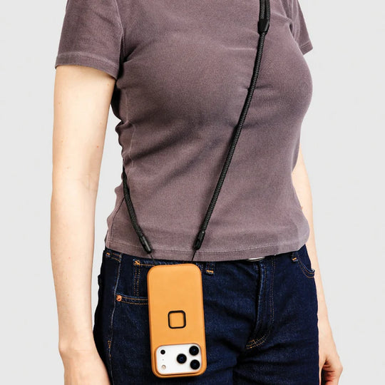 Person wearing a brown t-shirt with a black strap over the shoulder, holding a yellow phone case.