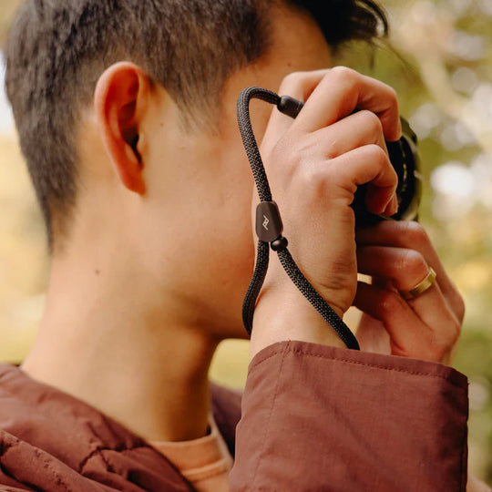 Person holding a camera with a peak design mobile cuff, blurred natural background