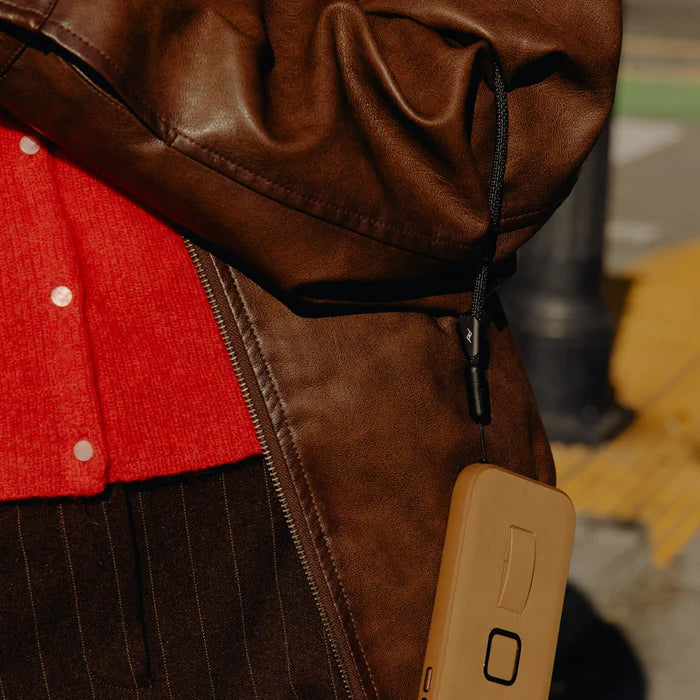 Close-up of a person wearing a brown jacket with a red shirt underneath, holding a beige device.