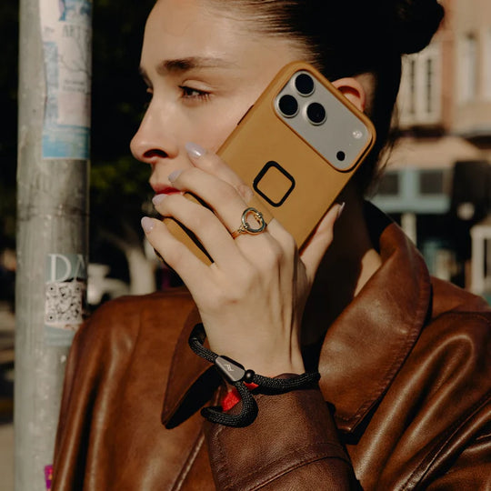 Person wearing a brown leather jacket holding a phone with a tan case.