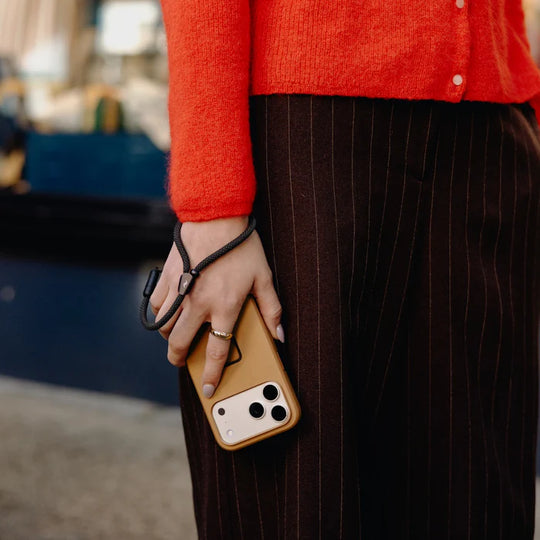 Person holding a phone with a brown case, wearing an orange sweater and dark pants.