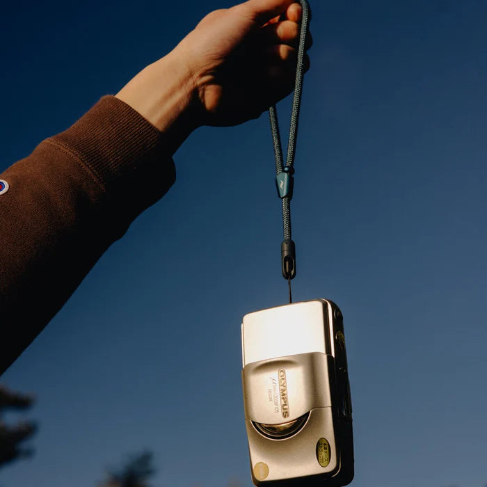 Gold camera with peak design mobile strap held against a blue sky