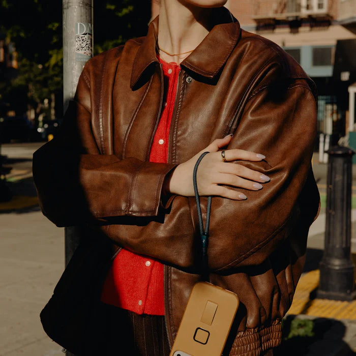 Person wearing a brown leather jacket over a red shirt, standing on a street.