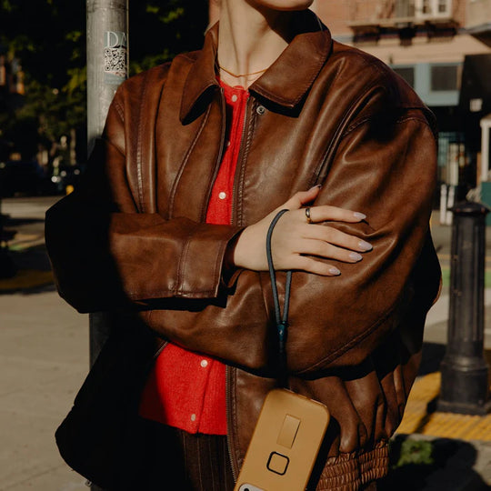 Person wearing a brown leather jacket over a red shirt, standing on a street.