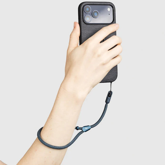 Hand holding a phone with a black case and Peak Design Mobile Cuff on a light gray background