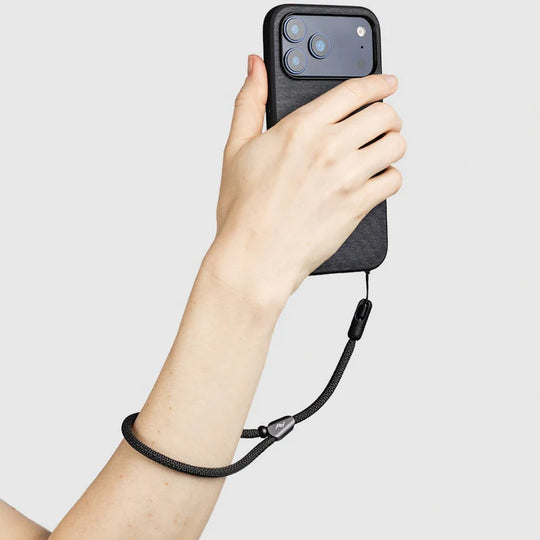 Hand holding a phone with a black case and peak design Mobile Cuff against a light gray background
