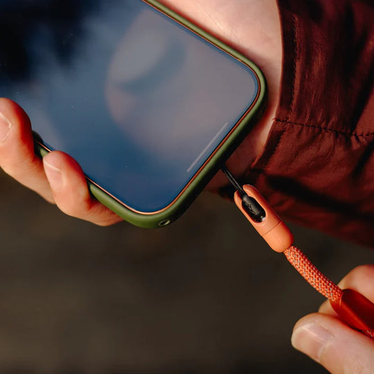 Person holding a smartphone with a green case and an orange mobile strap
