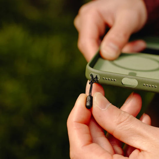 close up shot of hands attaching peak design mobile straps microanchor to a green phone case.