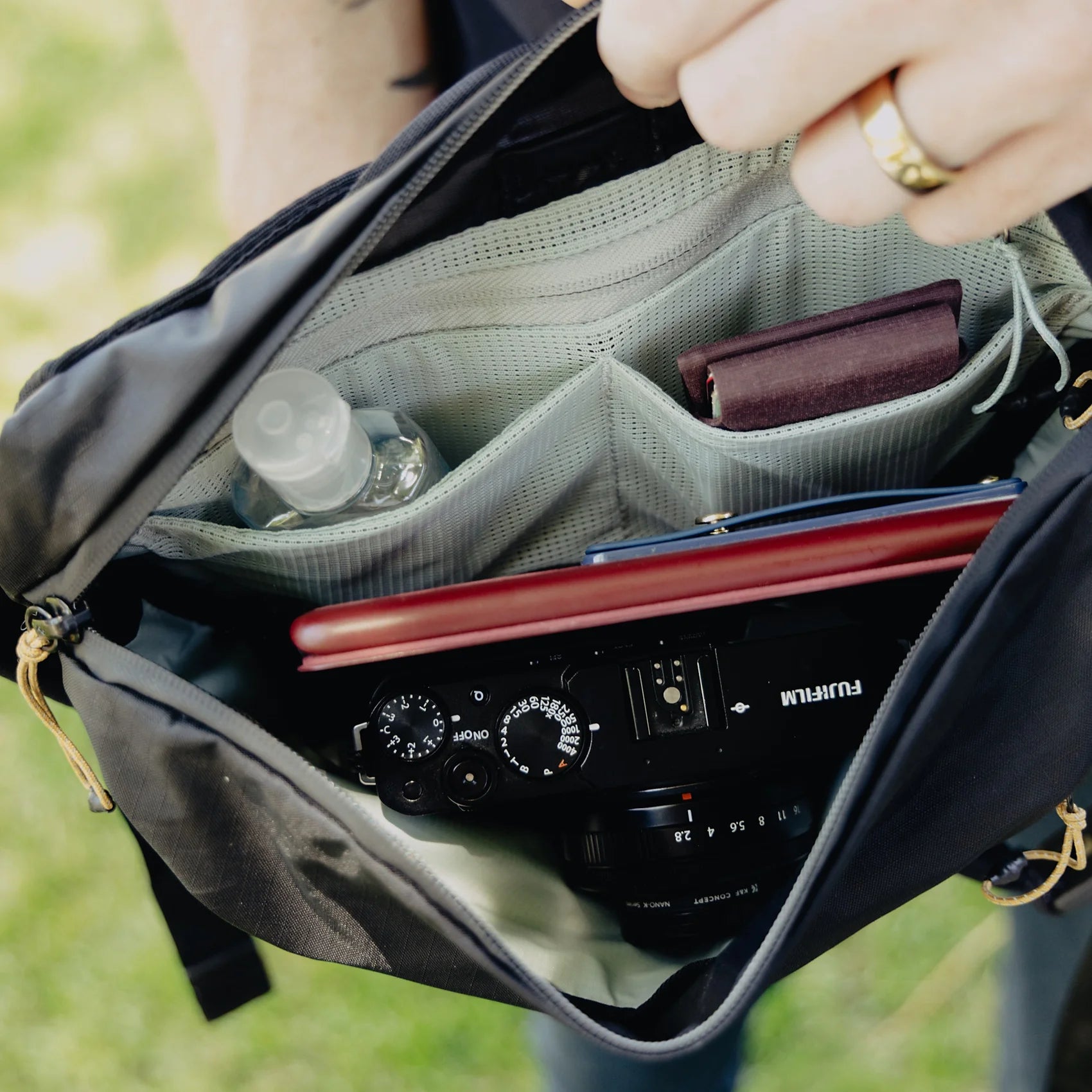 Person opening a bag to reveal a camera and other items on a grassy background