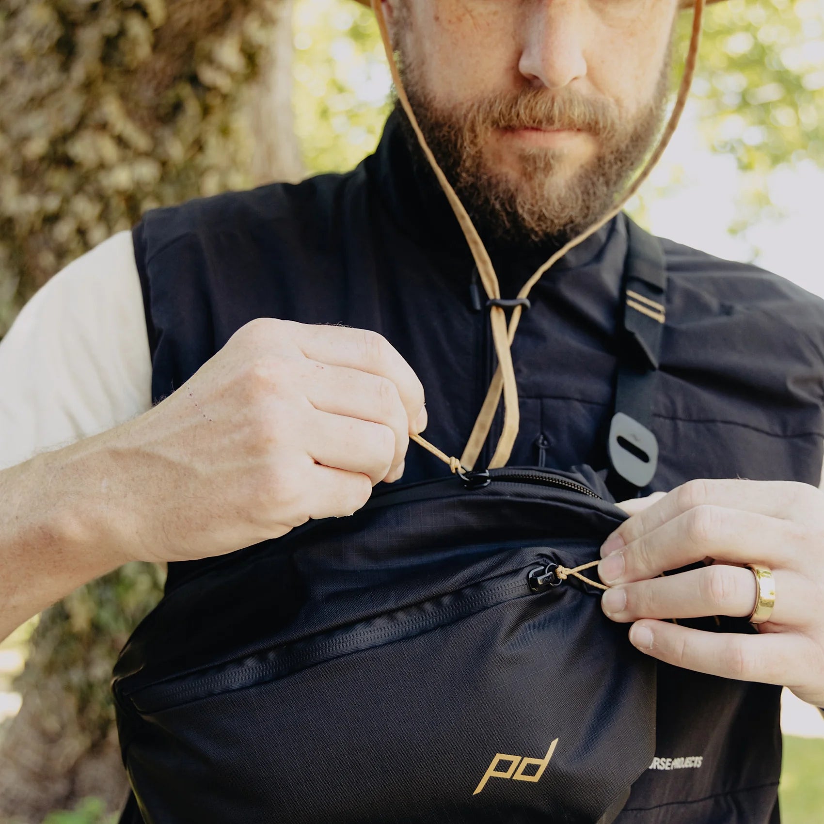 Man adjusting a black Outdoor Sling bag with a brand logo outdoors