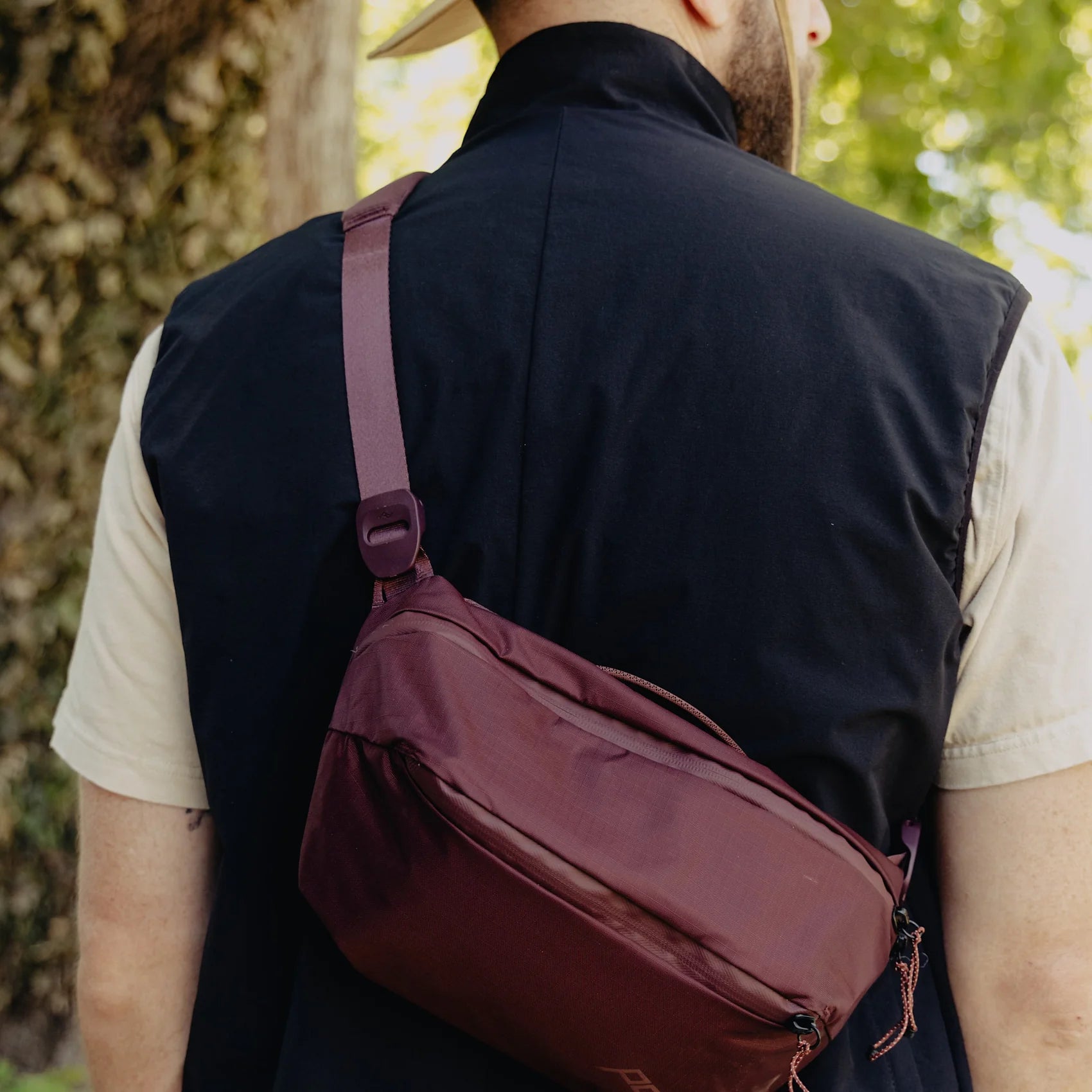 Person wearing a maroon crossbody bag outdoors with greenery in the background