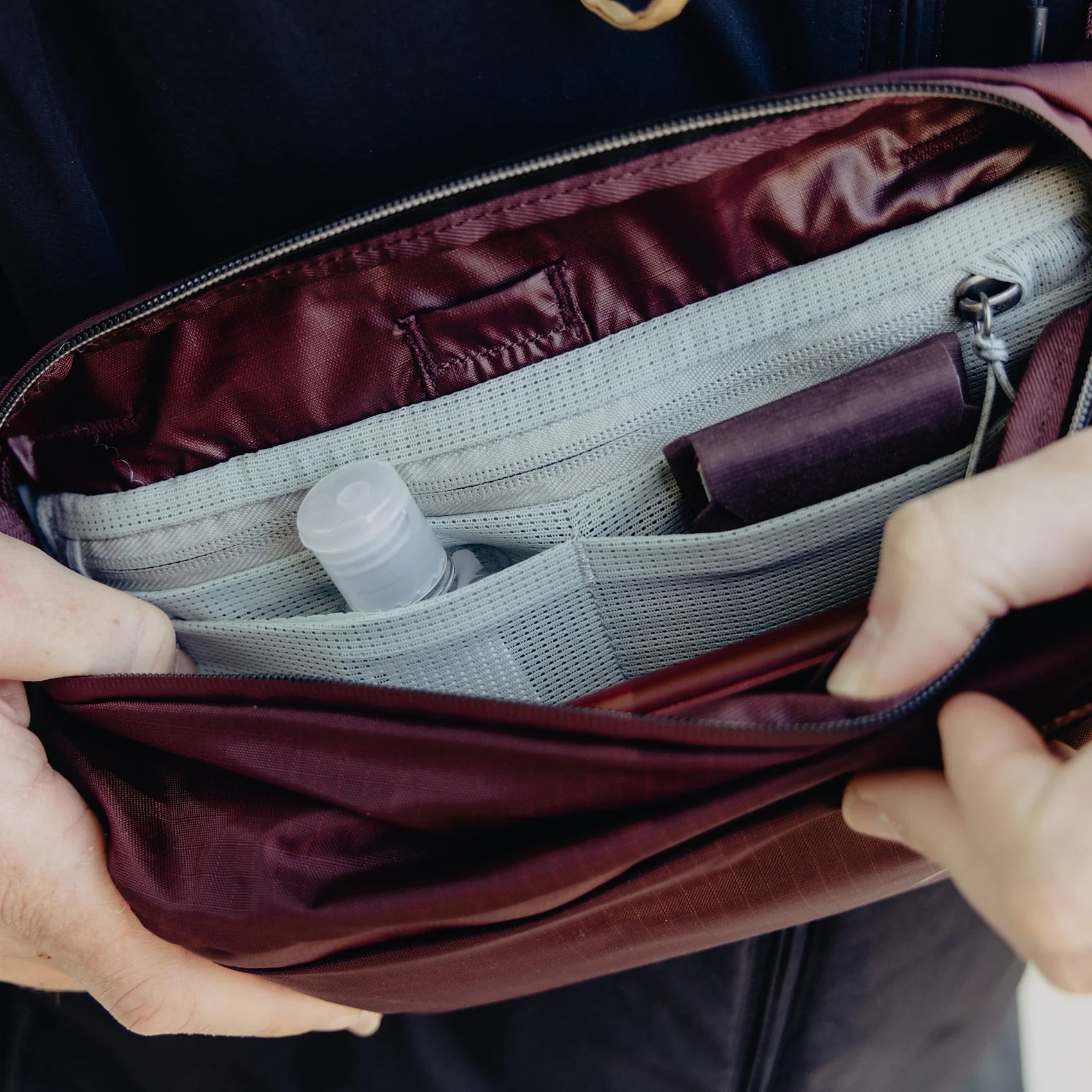 Person opening a maroon bag to reveal its interior with a water bottle and other items.