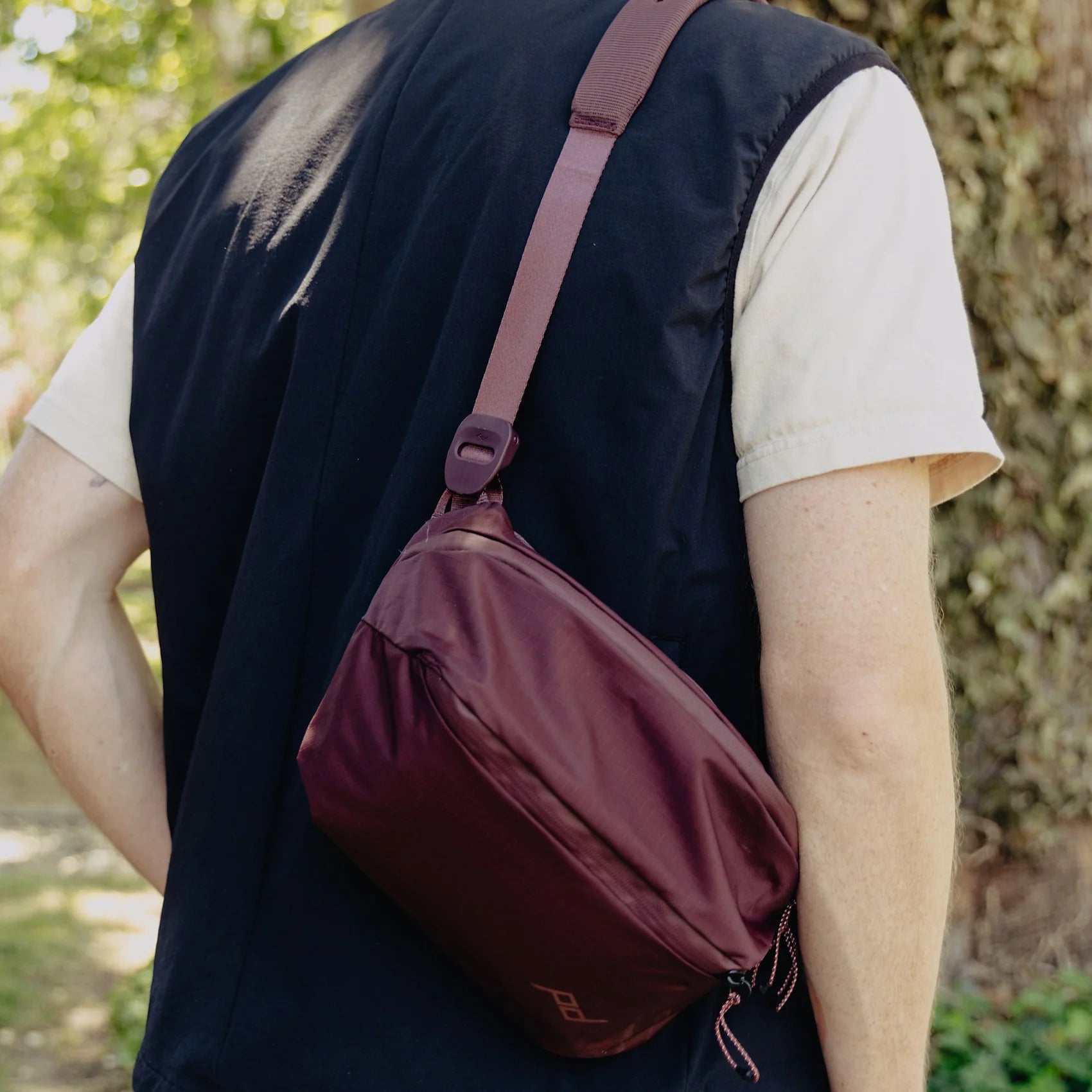 Person wearing a maroon crossbody bag outdoors
