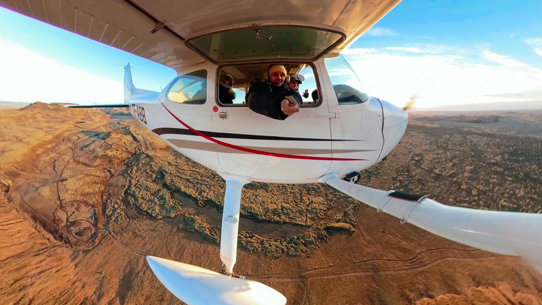 Small airplane flying over a desert landscape with a person inside.