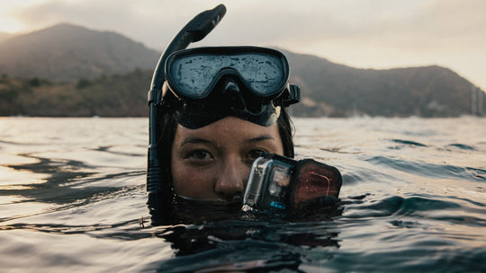 Person underwater with snorkel and camera, mountains in the background