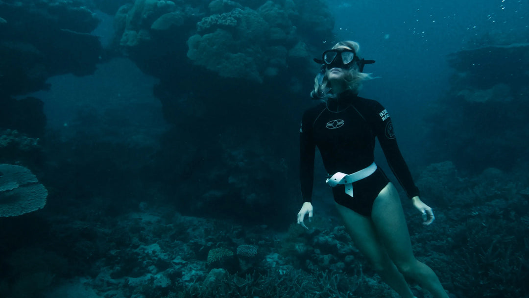 Person scuba diving in a dark underwater environment with coral.