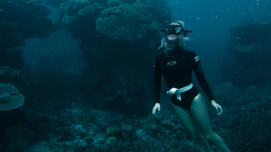Person scuba diving in a dark underwater environment with coral.