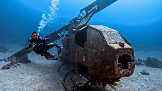 Diver exploring a large underwater object, possibly a shipwreck or mechanical structure, in clear blue water.